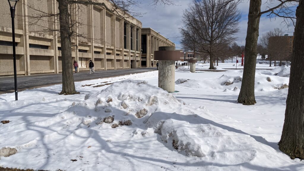 A view of Lanigan Hall and Penfield Library at SUNY Oswego; students walking on paved paths